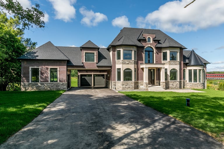 Large two-story brick home with turrets, arched windows, and attached garage on manicured lawn under blue sky